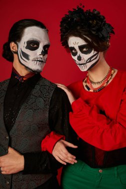 Catrina Calavera makyajlı korkunç bir çift kırmızıda kameraya bakıyor, dia de los muertos geleneği