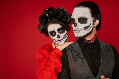 woman in catrina makeup and black wreath leaning on shoulder of eerie man on red, Day of Dead clipart