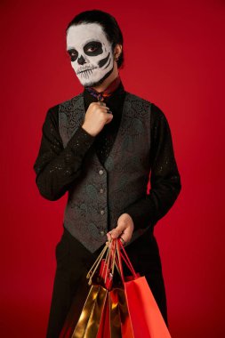 dia de los Muertos 'taki adam makyaj ve şık kıyafetler kırmızı sezonluk indirimli alışveriş torbalarıyla poz veriyor.