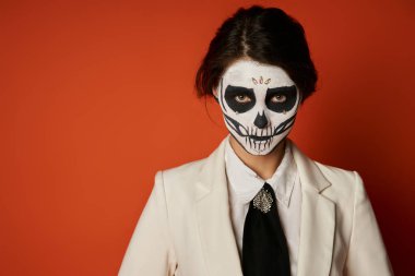 Catrina Calavera makyajlı ve şenlikli bir kadın kırmızı portrede kameraya bakıyor.