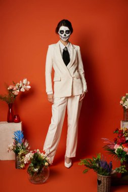 woman in skull makeup and white suit near traditional dia de los muertos ofrenda with flowers on red clipart
