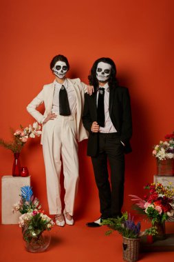 Şeker kafalı şık bir çift geleneksel dia de los muertos sunağı yakınında kırmızıda çiçeklerle