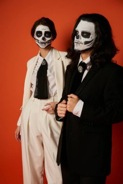 Catrina makyajlı bir kadın ve beyaz takım elbiseli bir kadın kameraya bakıyor.