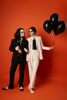 couple in catrina makeup and suits looking at each other near black balloons on red, Day of Dead clipart