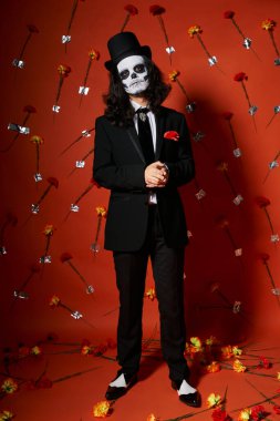 Kafatası makyajlı ve kırmızı çiçekli arka planda şenlikli bir adam, dia de los muertos
