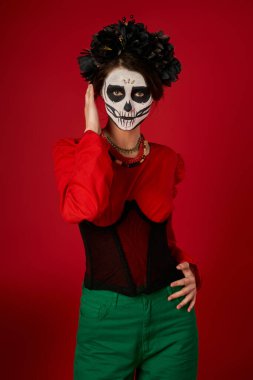 Geleneksel dia de los muertos kafatası makyajlı ve şenlikli kadın kırmızı kameraya bakıyor.