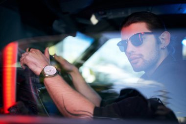 Arabasının direksiyonunda kol saati ve seksi bir sürücü ile poz veren yakışıklı genç bir adam.