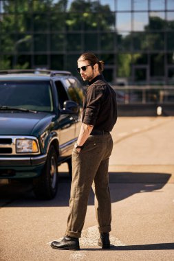 Zarif giyinmiş yakışıklı genç adam arabasının yanında duruyor ve başka tarafa bakıyor, moda anlayışı.