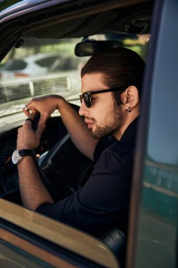 Şık görünümlü, şık bir erkek model arabasının direksiyonunda oturuyor, seksi şoför.