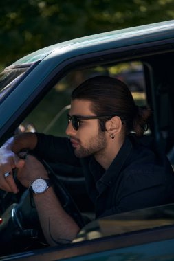 Küpeli, sakallı, siyah elbiseli, direksiyon başında yakışıklı, zarif bir adam. Seksi şoför.