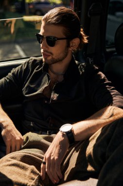 Dikey çekim, çekici genç erkek modelin şık görünümü arabasının arka koltuğunda ürpertici, moda.