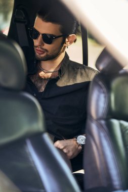 Güneş gözlüklü yakışıklı erkek model arabasının arka koltuğunda oturuyor, moda ve tarz.
