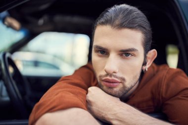 Kahverengi gömlekli yakışıklı moda adam elleri çenesinin altında kameraya bakıyor.