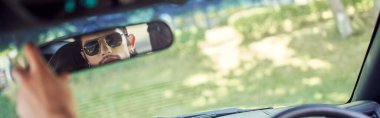 good looking young sexy man with stylish sunglasses looking at his rearview mirror, banner clipart