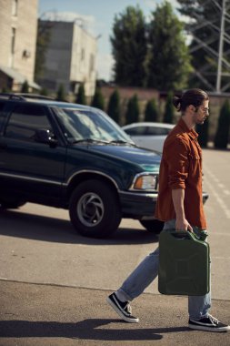 good looking sexy driver in brown shirt and jeans walking with petrol canister in his hands clipart