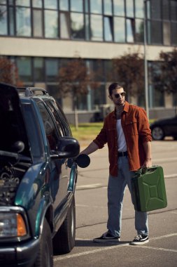 handsome sexy male model in brown shirt and jeans with elegant sunglasses refueling his car clipart