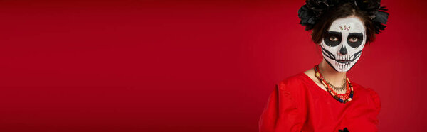 portrait of scary woman in traditional dia de los muertos makeup and colorful beads on red, banner