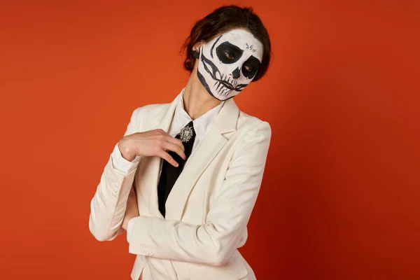 stock image woman in spooky sugar skull makeup and white elegant blazer posing on red, dia de los muertos fest