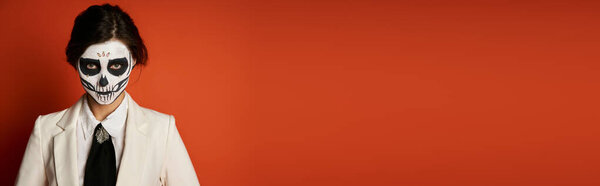 portrait of woman in scary sugar skull makeup and festive attire looking at camera on red, banner