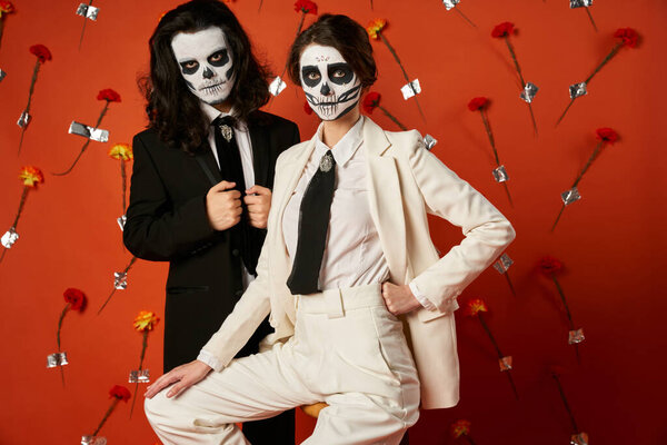 couple in catrina makeup and elegant attire posing on red background with flowers, Day of Dead