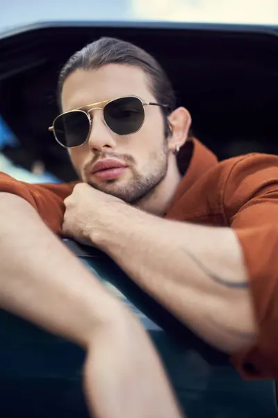 良い見栄えのスタイリッシュな男性モデル クロスアームで彼の車にポーズするサングラス 顔の近くの手 — ストック写真