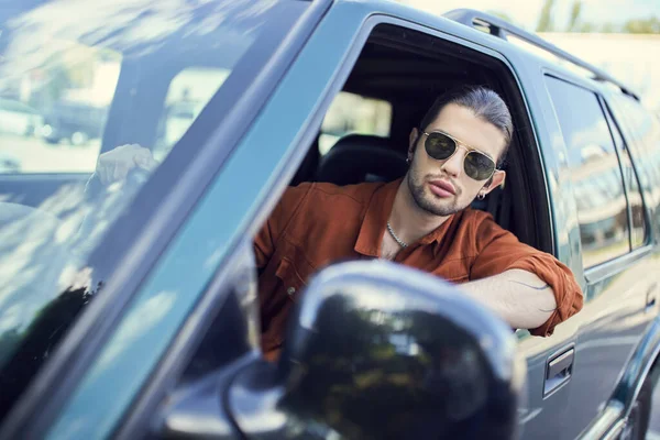 handsome young man in trendy outfit with accessories looking out of car window, sexy driver