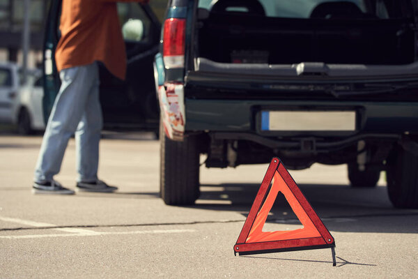 cropped view of young stylish man standing next to his car with warning triangle, blurred photo