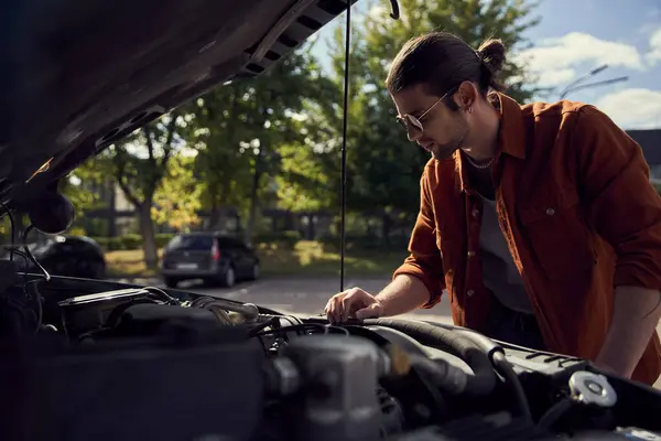 stock image pensive handsome man in stylish outfit with sunglasses and ponytail checking on his car engine