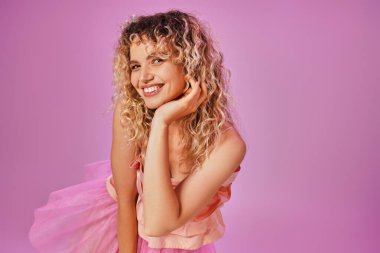 close up of joyous lovely woman in pink outfit smiling sincerely at camera with hand raised to face clipart