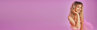 Pembe kostümlü neşeli kadın kameraya samimi bir şekilde gülümsüyor.