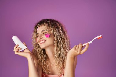 portrait of happy blonde woman with curly hair and face stickers holding toothbrush and paste clipart