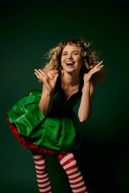 cheerful curly woman dressed as new year elf smiling happily at camera with hands raised face clipart