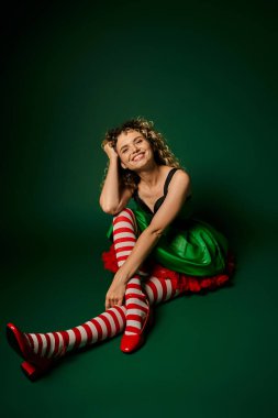 happy woman in festive dress with striped stockings smiling at camera, new year elf concept clipart