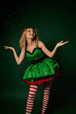 Mutlu yeni yıl elfi, şenlikli kıyafetiyle yeşil arka planda kar altında poz veriyor.