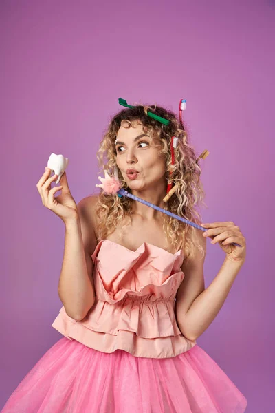 stock image cheerful tooth fairy in pink outfit casting spell on tooth with magic wand posing on pink backdrop