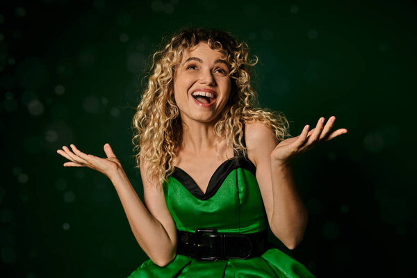 cheerful woman in new year elf costume looking at snow and catching snowflakes on green background