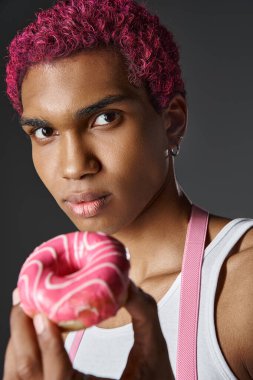 Pembe saçlı genç Afro-Amerikan bir adamın portresi. Pembe donut, moda ve tarz ile poz veriyor.