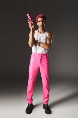 stylish african american man with pink hair pointing up his pink toy gun posing on gray backdrop clipart
