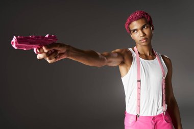 Pembe pantolonlu, aksesuarlı, pembe oyuncak tabancasını bir kenara çeken yakışıklı, pembe saçlı şık adam.