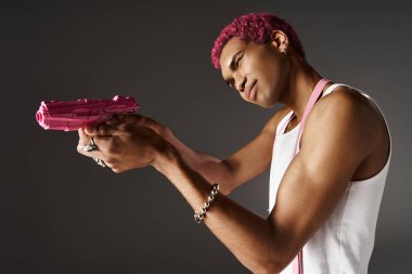 Pembe saçlı Afro-Amerikan pantolonlu erkek manken pembe oyuncak silahını bir tarafa doğrultuyor.