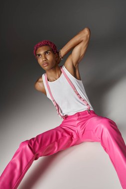 Pembe saçlı, güzel bir erkek model. Elleri boynun arkasında yerde oturuyor. Moda anlayışı.