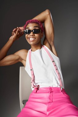 playful young man with pink hair and suspenders smiling wearing sunglasses, fashion concept clipart