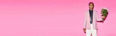 Pembe saçlı şık Afrikalı Amerikalı adam pembe arkaplanda gül buketi ile poz veriyor.