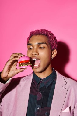 Pembe ceketli şık görünümlü adam pembe fırında doğal olmayan bir şekilde mini burger yiyor.
