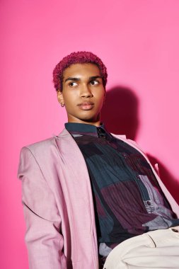 good looking man with curly pink hair posing on pink backdrop and looking away on pink backdrop clipart