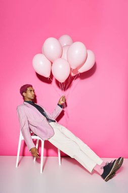 handsome young male model posing unnaturally with balloons in hand on pink backdrop, doll like clipart