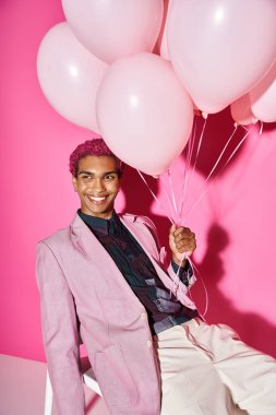 good looking man with curly pink hair posing on white chair with balloons in hand, doll like clipart