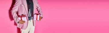 cropped view of stylish young man in vibrant outfit with presents in hands on pink backdrop, banner clipart