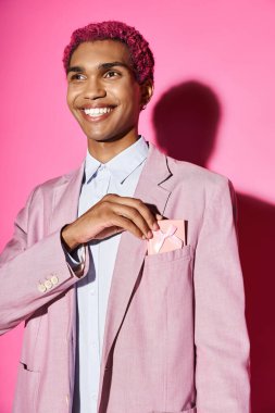 young pink haired male model in vibrant clothes smiling unnaturally with present in his pocket clipart
