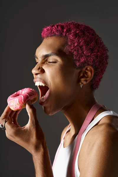 Pembe saçlı, gümüş aksesuarlı yakışıklı adam pembe donut yiyor, moda ve tarz.